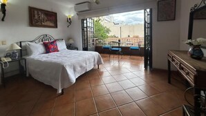 Un dormitorio con cama, mesita de noche, escritorio, silla y balcón con vistas.