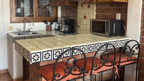 Una cocina con armarios de madera, salpicadero de azulejos, una isla de ladrillo, una silla metálica y una lámpara colgante.
