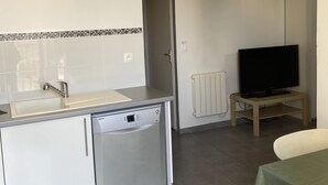 A compact kitchen with a dishwasher, a small sink, and a television on a wooden stand.