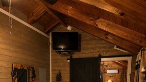 Acogedor interior de una cabaña de madera con una cama, un aparador de madera y un televisor montado en la pared.