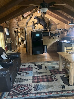 L’intérieur d’un chalet rustique, avec un plafond en bois, un réfrigérateur noir, une table à manger, un canapé et un tapis à motifs.
