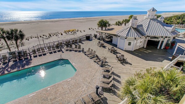 A pool area with lounge chairs and a view of the beach.