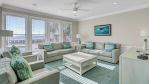 A spacious living room with a large window, a ceiling fan, and a view of the ocean. - 131 Grand Pavilion by Avantstay Oceanfront On The Boardwalk! (Isle of Palms)