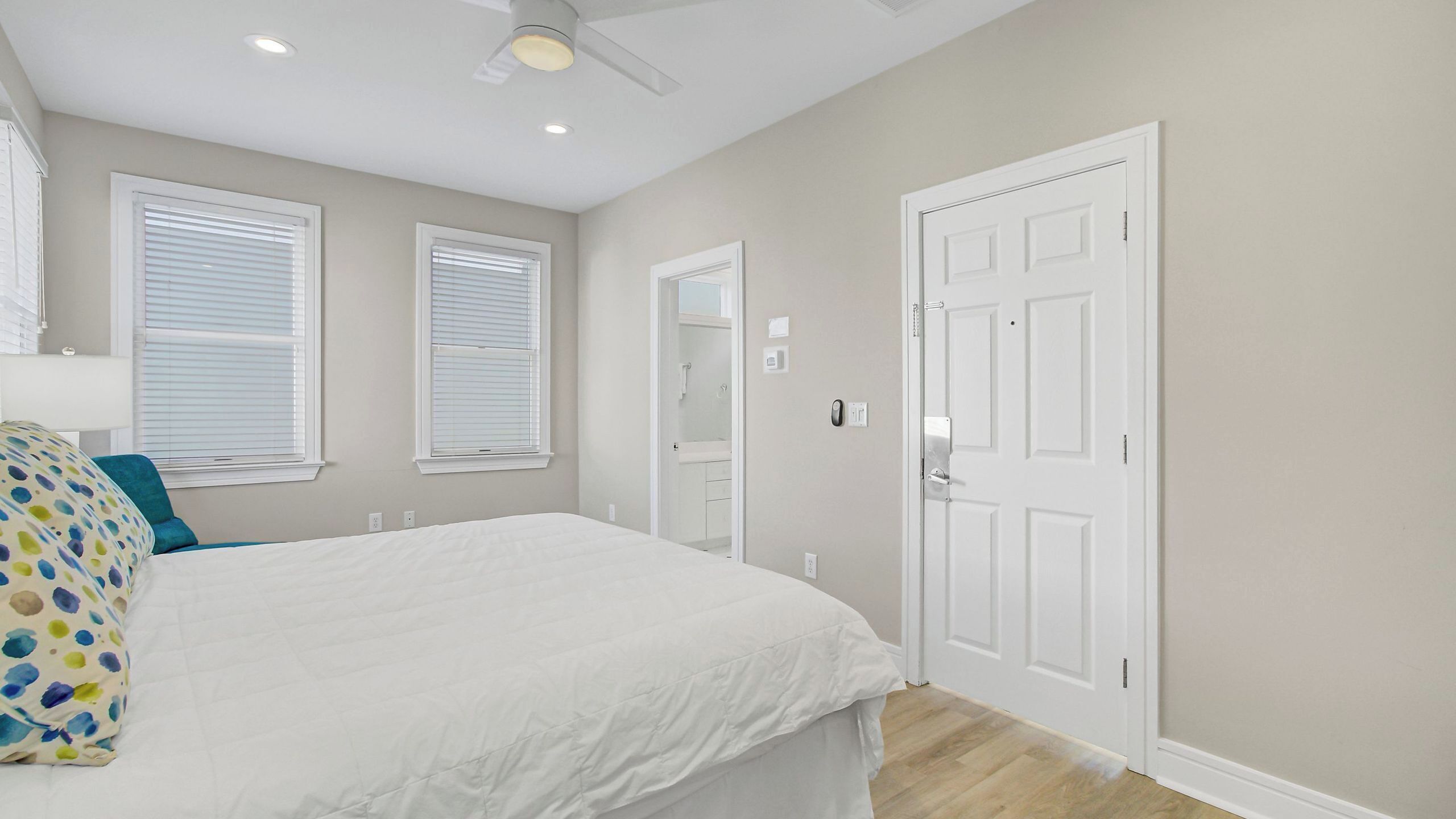 A bedroom with a bed, two windows, a door, and a ceiling fan.