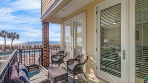 A balcony with wicker furniture, a glass door, and a view of the ocean. - 131 Grand Pavilion by Avantstay Oceanfront On The Boardwalk! (Isle of Palms)