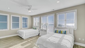 A bedroom with two beds, a ceiling fan, and large windows with blinds.