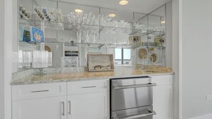 Een keuken met een roestvrijstalen vaatwasser, een marmeren aanrechtblad en een glazen vitrine met diverse glazen.