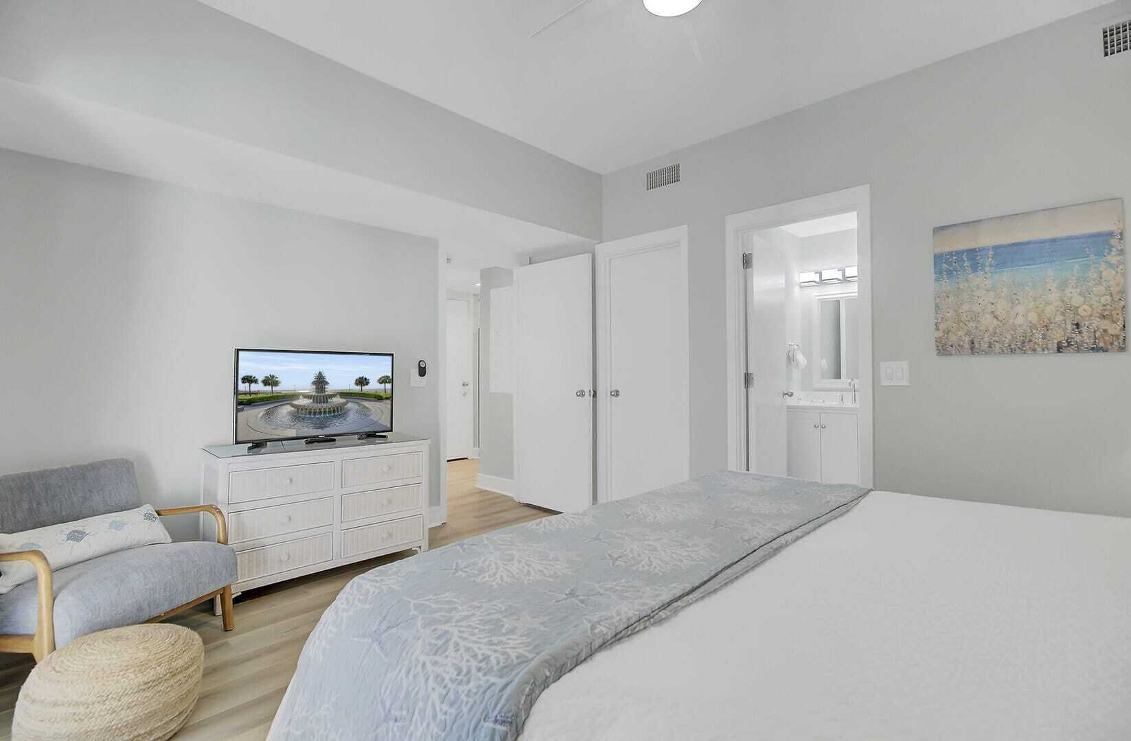 A bedroom with a bed, a TV on a dresser, a chair, and a painting on the wall.