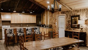 A rustic kitchen with wooden cabinets, a central island, and a dining area with a wooden table and chairs.