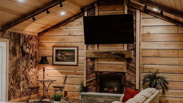 A cozy log cabin interior with a fireplace, a mounted television, and a dining area.
