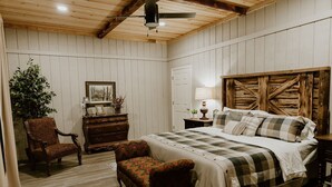 A bedroom with a wooden ceiling, a bed with a checkered bedspread, a wooden headboard, a dresser, a chair, and a lamp.
