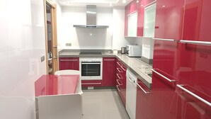 Une cuisine de taille réduite avec des meubles rouges, un plan de travail blanc, un four encastré et un four à micro-ondes.