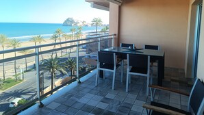 Un balcon avec une table et des chaises, donnant sur une plage et l’océan.