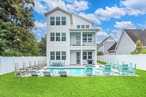A two-story house with a swimming pool, outdoor seating, and a white fence.