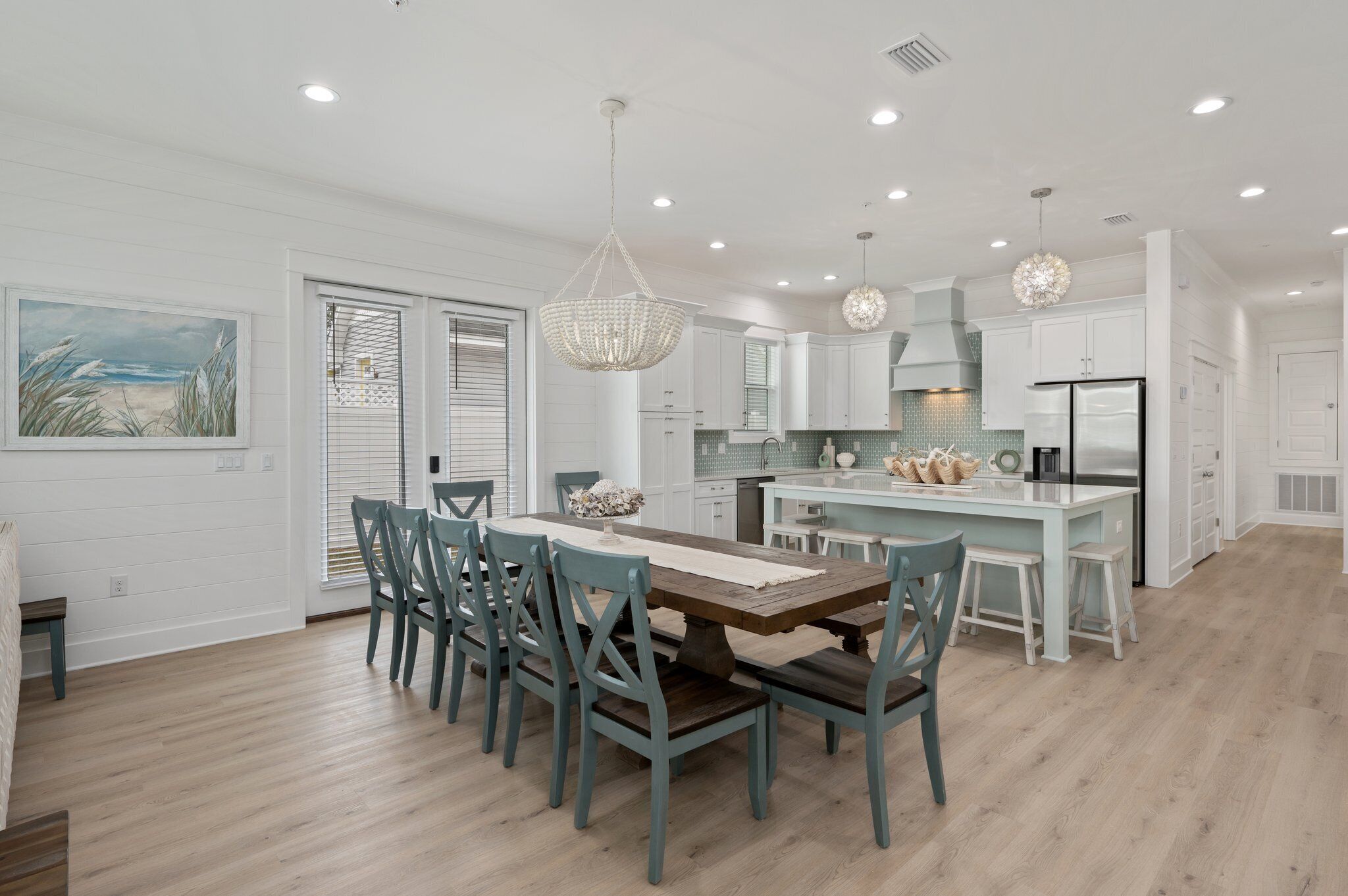 A modern kitchen with white cabinetry, a central island, and a dining area with a wooden table and blue chairs.