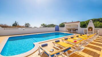 A swimming pool with sun loungers and a covered area with a table and chairs.