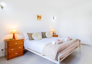Un letto ben rifatto con un piumone bianco e beige, due comodini con lampade e un fiorile a parete.