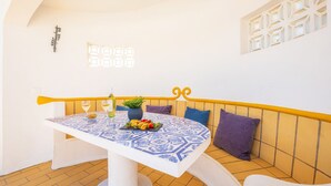 A dining area with a table set for two, a bench with cushions, and a decorative wall with a geometric pattern. - Villa with heatable pool & BBQ, Carvoeiro (Carvoeiro)