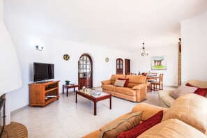 A living room with a television, sofa, coffee table, and a dining area with chairs and a table.
