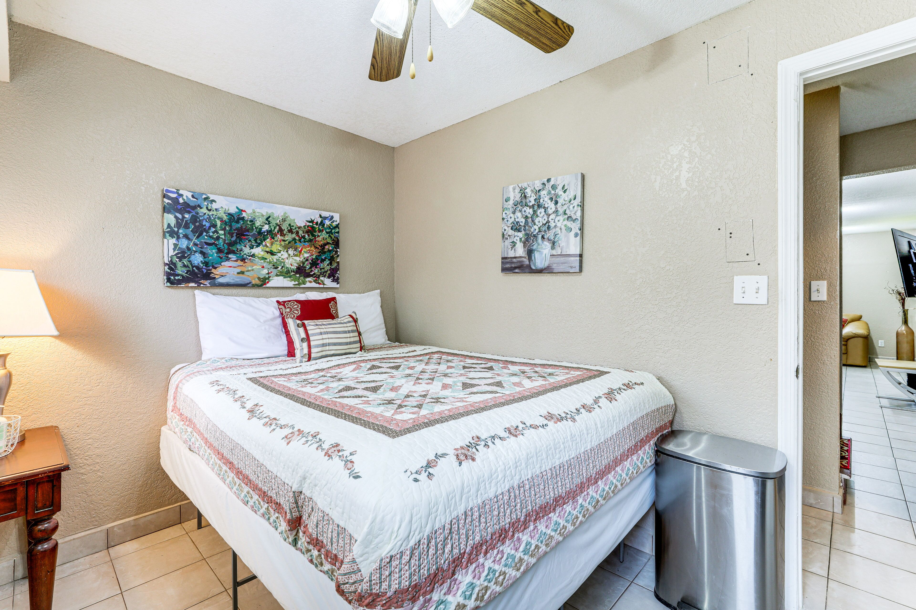 Ein Schlafzimmer mit einem Bett, einem Nachttisch, einem Mülleimer und zwei Bildern an der Wand.