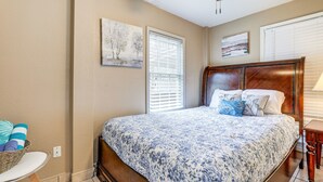 A bedroom with a large bed, a wooden headboard, a bedside table, a wall-mounted artwork, and a window with blinds. - Pet-Friendly Lilburn Duplex w/ Patio & Grills! (Lilburn)