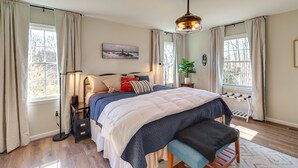 A bedroom with a bed, bedside lamp, and a view of the outdoors through large windows. - Peaceful Queenstown Home w/ Deck & Grill! (Queenstown)