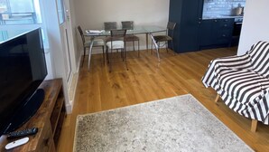 A living room with a TV, a sofa, a dining table with chairs, a kitchen in the background, and a framed picture on the wall. - Delightful & Well-located 2BD Flat Central Pimlico (London)