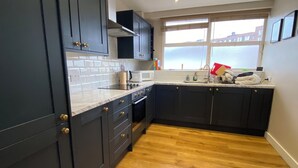 A modern kitchen with dark cabinetry, a white countertop, and a wooden floor. - Delightful & Well-located 2BD Flat Central Pimlico (London)