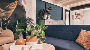 A cozy living room with a blue sofa, a pink ottoman, and a white side table with a plant.