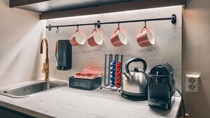 A modern kitchen with a marble countertop, a stainless steel kettle, a tea box, and a hanging rack with cups.