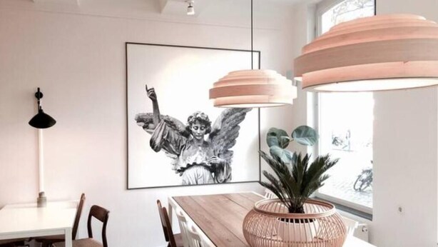 A modern dining area with a wooden table, chairs, a large framed artwork, and a potted plant.