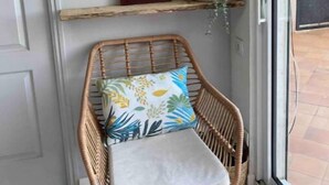A wicker chair with a cushion and a framed picture on a shelf, a hanging plant, and a 'welcome' sign. - Joli Mas T3 vue Mer. Animaux de Compagnie Acceptés ! (Istres)