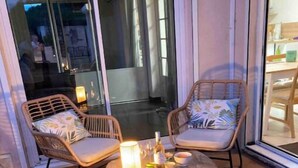 A patio area with wicker chairs and a small table, featuring a glass door leading to an outdoor space. - Joli Mas T3 vue Mer. Animaux de Compagnie Acceptés ! (Istres)