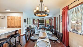 Un coin repas avec une table en bois dressée pour quatre personnes, un lustre et une cheminée en arrière-plan.