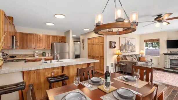 Una cucina moderna con mobili in legno, un'isola centrale e un'area pranzo per sei persone illuminata da un lampadario.