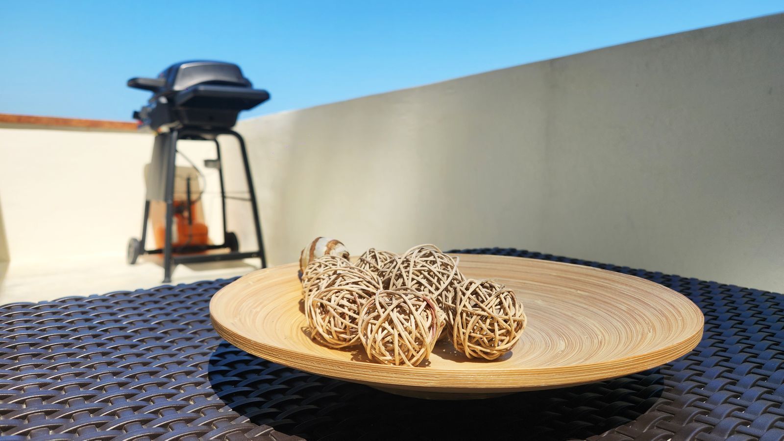 A wicker ball on a round wooden tray on a metal table.