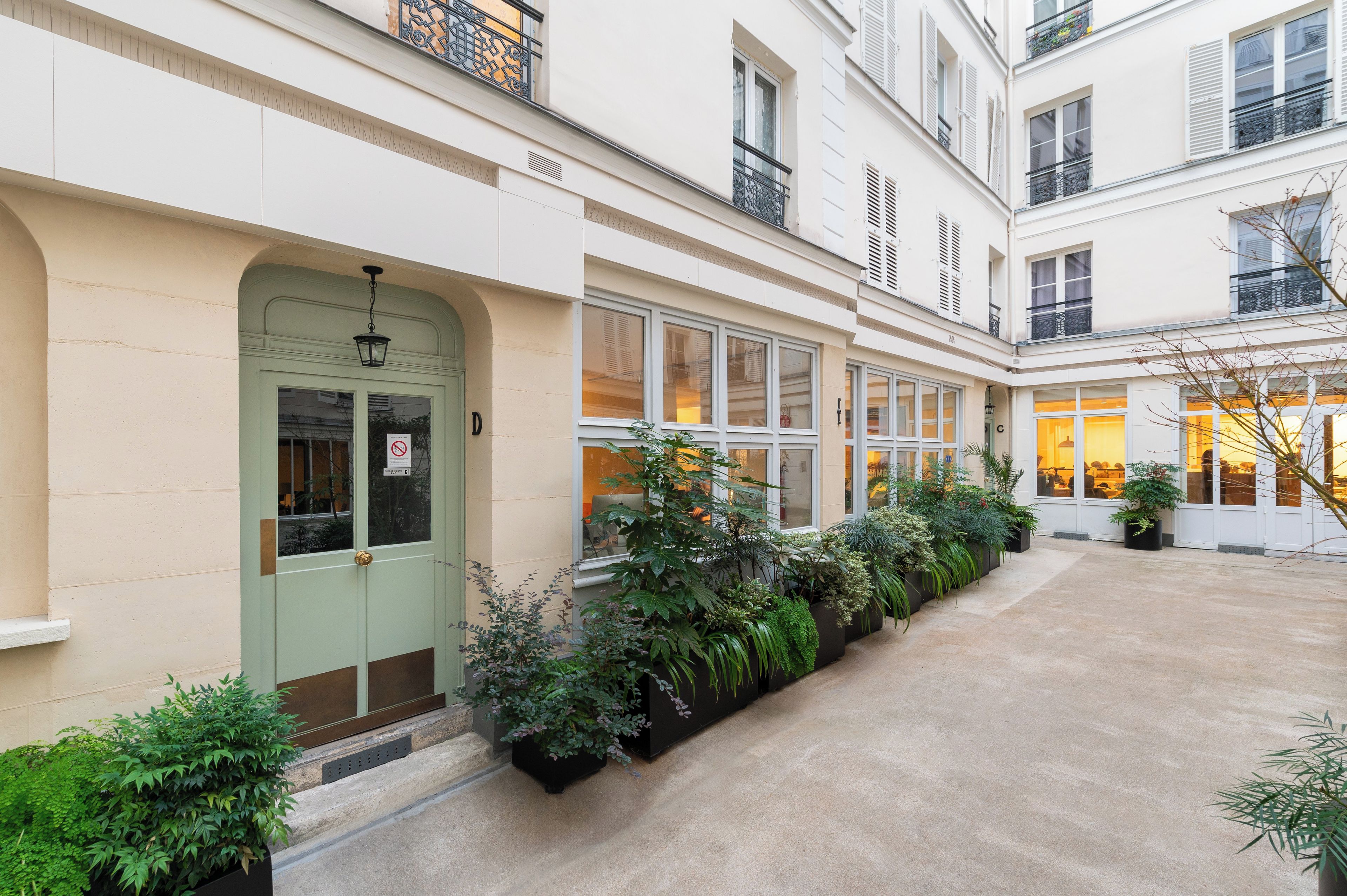 A building with a green door, multiple windows, and a courtyard with potted plants.