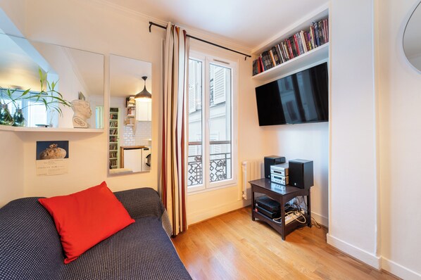 A cozy room with a bed, a TV, a bookshelf, and a window with curtains.