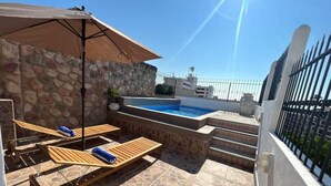 A rooftop pool area with stone walls, a small pool, and wooden lounge chairs.