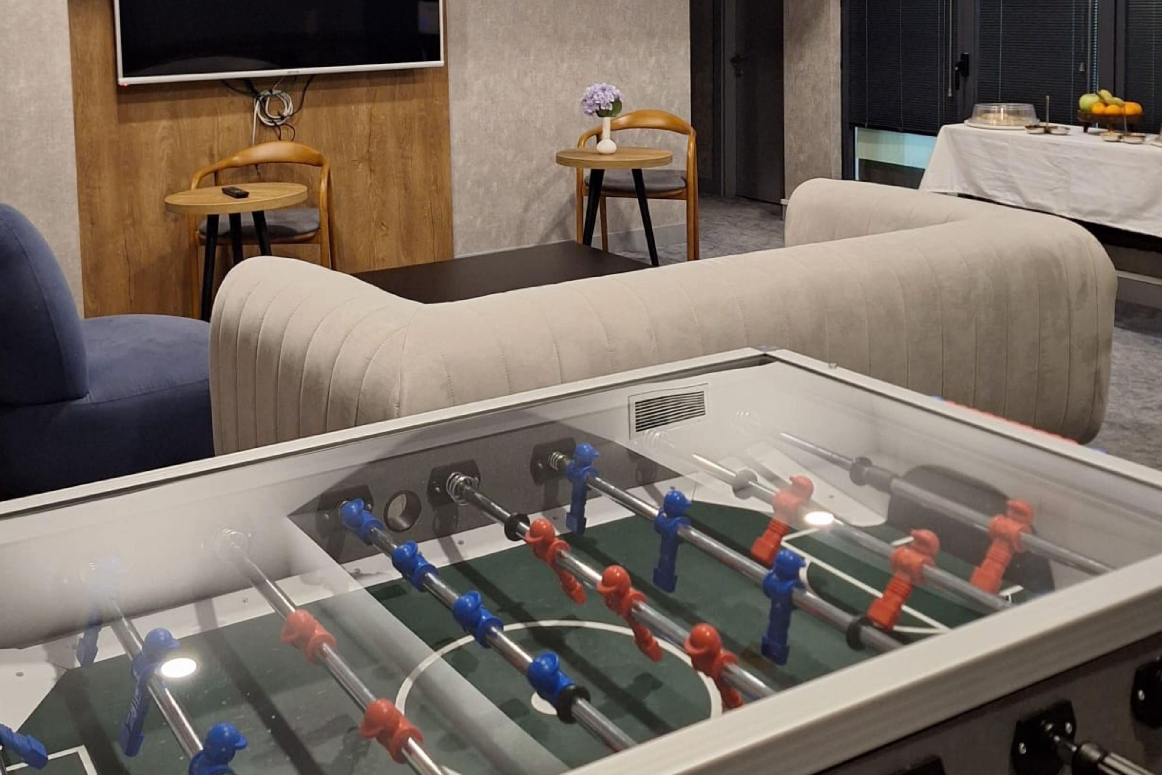 Quarto com mesa de futebol, sofás, televisão e uma pequena mesa com um vaso.