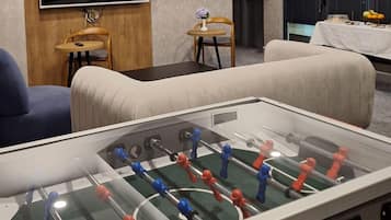 Quarto com mesa de futebol, sofás, televisão e uma pequena mesa com um vaso.