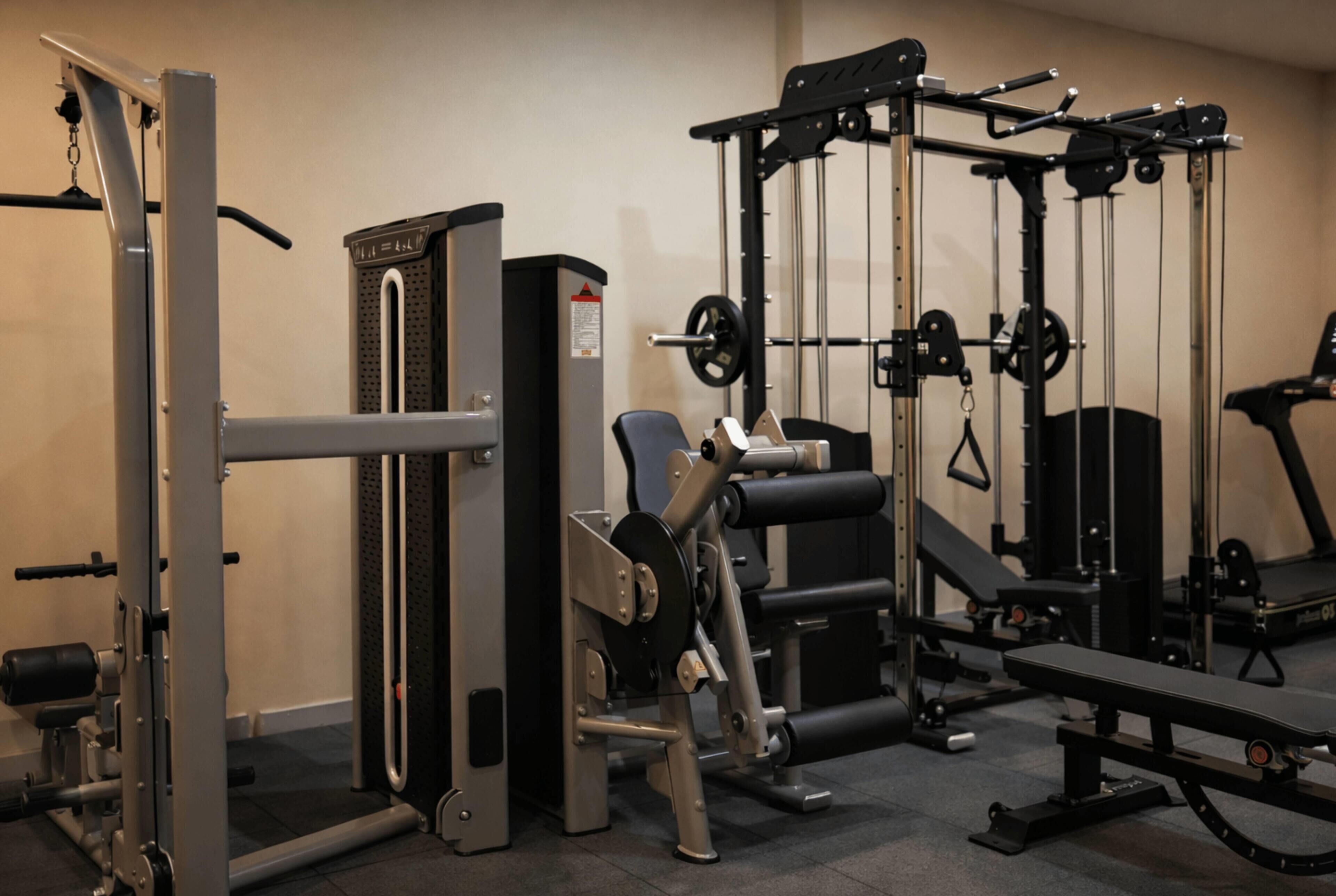 Une salle de sport équipée de divers appareils d’entraînement, notamment un support à squats, un banc de développé couché et des machines de musculation.