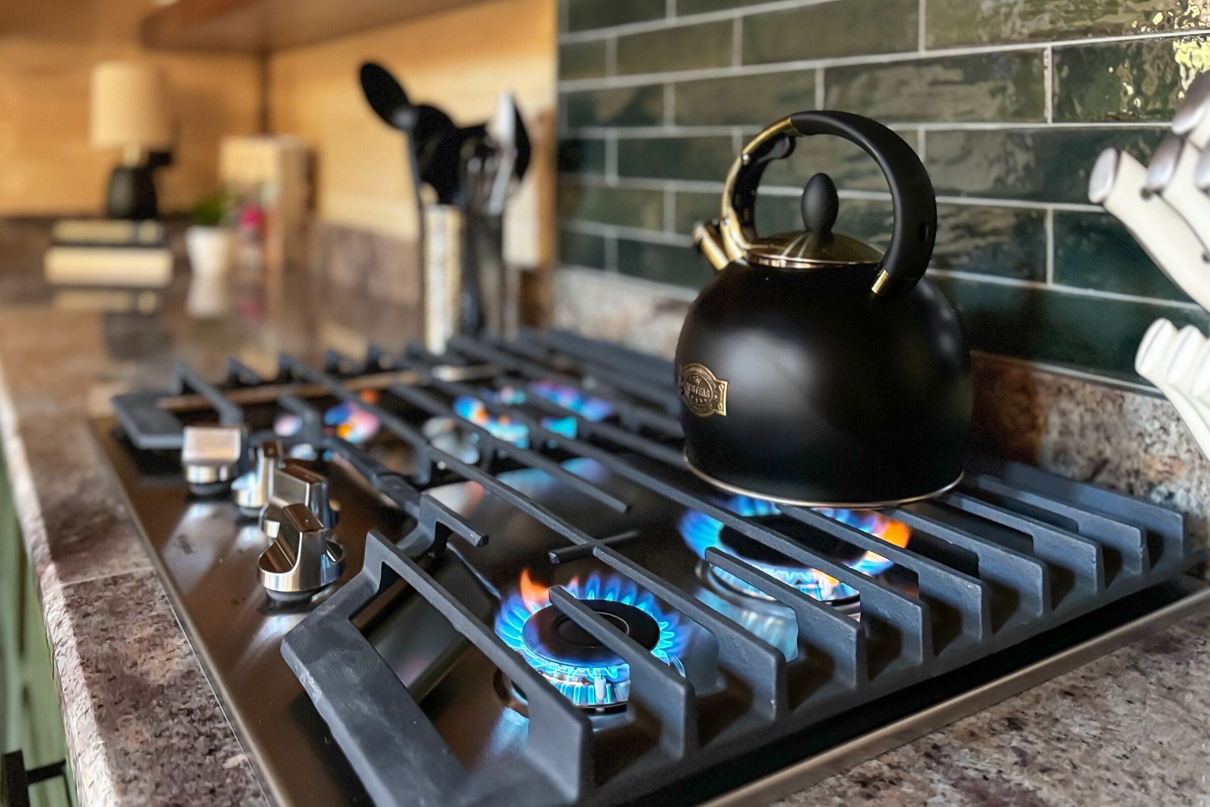 Una cocina con estufa a gas, hervidor y salpicadero de azulejos.