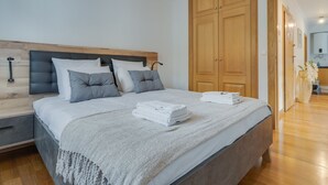 A neatly made bed with a grey headboard, a wooden wardrobe, and a wooden floor. - Encanto Santa Cruz (Santa Cruz)