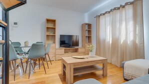 A modern living room with a wooden coffee table, grey chairs, a flat-screen TV, and built-in wooden shelving. - Encanto Santa Cruz (Santa Cruz)