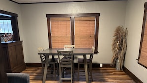 Un coin repas avec une table et des chaises en bois, une fenêtre avec des stores et une plante décorative.