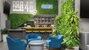 Un espace bar agrémenté d’un mur végétal, de chaises bleues, d’un comptoir et d’une grande plante en pot.