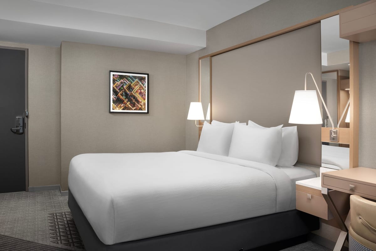 A hotel room with a large bed, bedside tables, a mirror, and a framed artwork on the wall.