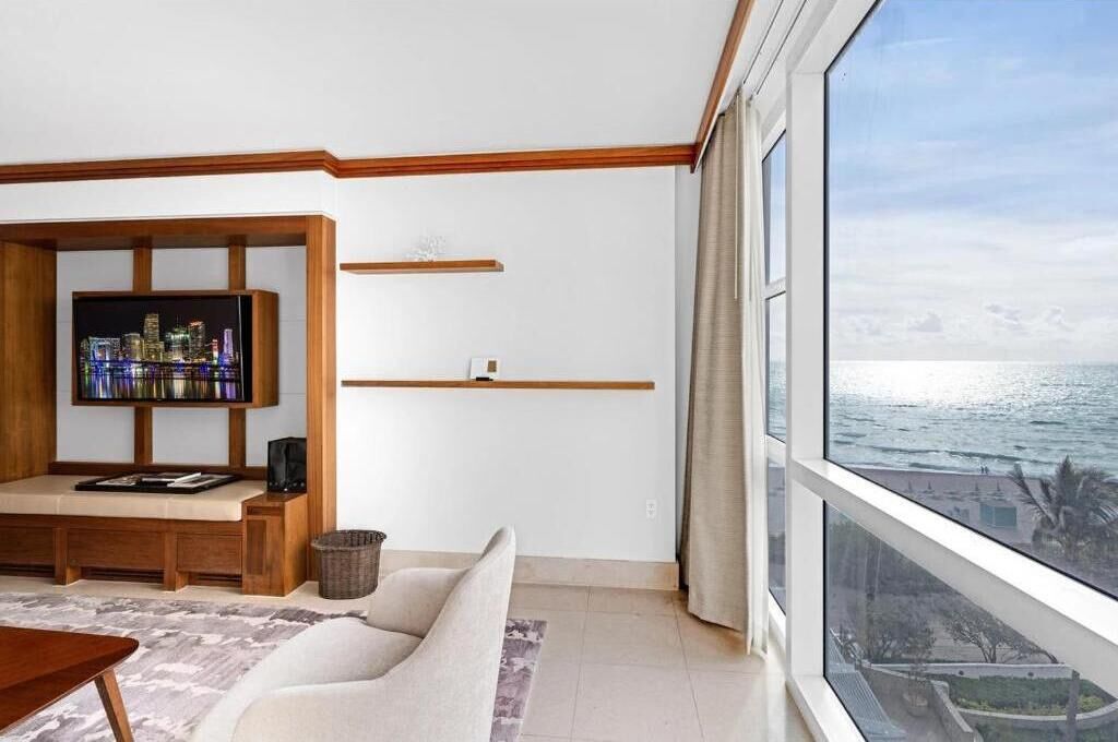 A modern living room with a large window overlooking the ocean, a built-in TV, and a minimalist design.