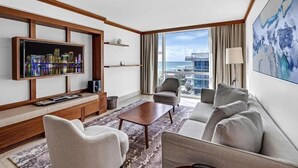 A modern hotel room with a large TV, comfortable seating, a view of the city, and a large window.